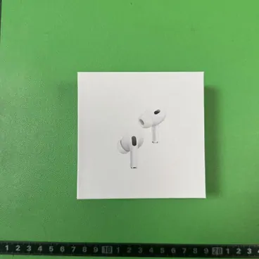 A boxed pair of wireless earbuds photographed on a green cutting mat